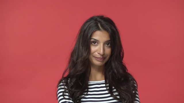 Silly feminine and sensual indian woman with dark long hairstyle, shifting eyes sideways and down, smiling acting arrogant and snobbish, knowing own worth, flirting, standing red background
