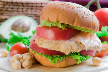 Burger with salmon and hummus on vegetable background