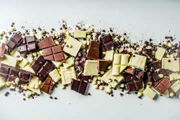 Assorted different types of chocolate. Broken pieces of dark, milk and white chocolate, with nuts, cooking chocolate, shavings. top view copy space