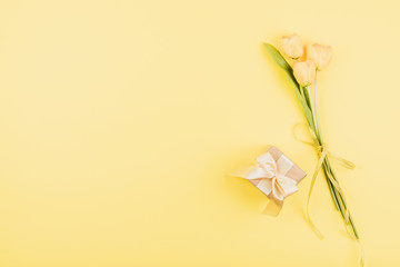 Fototapeta premium Yellow tulips flowers and gift box on pastel background. Festive birthday flat lay. Greeting for Womens or Mothers Day.