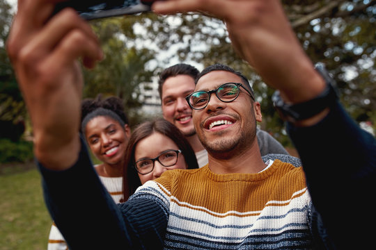 Smiling American Brazilian man taking selfie on mobile phone enjoying time together with his friends