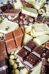 Assorted different types of chocolate. Broken pieces of dark, milk and white chocolate, with nuts, cooking chocolate, shavings. top view copy space
