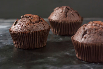 Three chocolate muffins on a black plate on a dark background close up