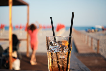 hand close-up holding Colorful glass cocktail at sunset at the beach with dancing girl and blurred background.