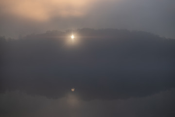 Reflection of the first rays of the sun in a misty forest lake