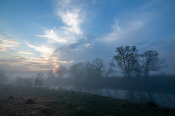 Reflection of the first rays of the sun in a misty forest lake