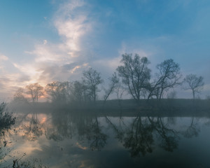 Reflection of the first rays of the sun in a misty forest lake