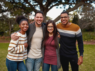 Portrait of a smiling diverse group of young friends standing together in the park outdoors on a...