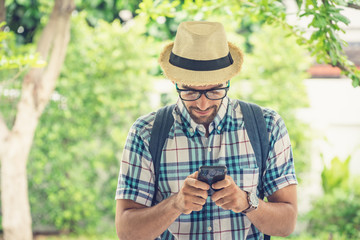 Happy young bearded wearing eye glasses man carrying his backpack preparing to travel. searching the map on mobile phone.