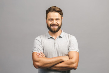 Happy young man. Portrait of handsome young man in casual shirt keeping arms crossed and smiling while standing against grey background - Powered by Adobe