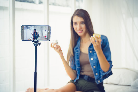 Young beauty blogger selling her cosmetic on live stream broadcasting by mobile phone.