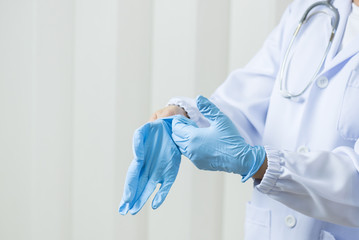 Woman doctor putting blue latex medical gloves on white wall background.Surgeon wearing gloves before surgery at operating room.Risk management protection health care concept.