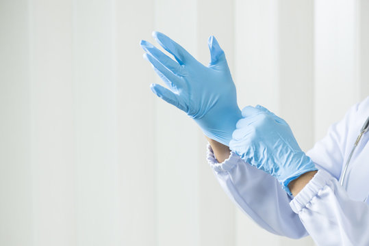 Woman doctor putting blue latex medical gloves on white wall background.Surgeon wearing gloves before surgery at operating room.Risk management protection health care concept.