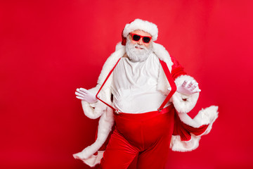 Portrait of style fat overweight santa claus with big funny belly abdomen touch his suspenders overalls posing like a model wearing trousers pants isolated over red background