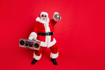 Full length photo of cheerful santa claus in headwear hat holding boom box glittering ball dancing...