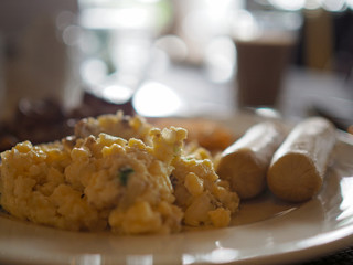 Closeup of scrambled egg and sausage with blurred coffee background. Selected focus.