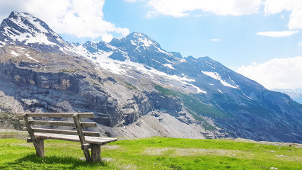 Beautiful natural landscape, summer mountain landscape over the snowy mountain range dolomite italy with wooden bench and green meadow in nature background.