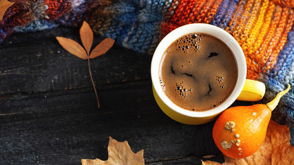 Yellow espresso coffee Cup on wooden table with autumn leaves, pumpkin and colorful autumn warm scarf . Warmth and comfort . Copy space