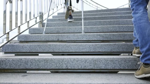 Young man with one leg on crutches with skateboard climbs the stairs faster than his friend. Active life of disabled person. The guy without leg enjoying his life. Motivation, never give up