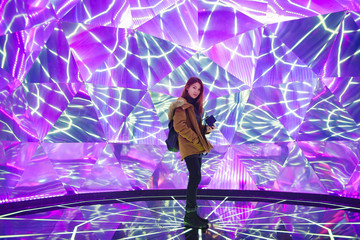 Young asian woman traveler posing on the stage with neon colored lights in background.