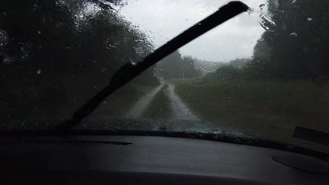 Driving car on forest path during hail with moving wipers