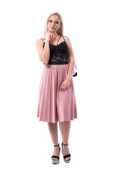 Young blonde smart woman with glasses looking at camera thinking with finger on chin. Full body isolated on white background.