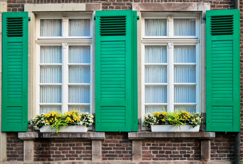 Two retro windows with green wooden shades with yellow flowers on red brick building