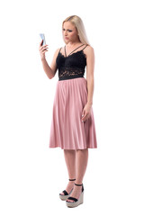 Doubtful displeased young blond woman reading news on mobile phone with angry expression. Full body isolated on white background.