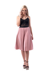 Happy relaxed young blonde stylish woman walking and speaking on the mobile phone looking down. Full body isolated on white background.