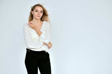 Portrait of a pretty blonde girl in a white blouse on a white background. Right in front of the camera in various poses.