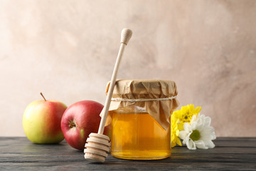 Glass jar with honey, dipper, apples and flowers on wooden background, space for text
