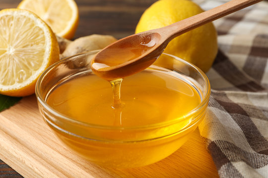 Lemons, bowl with honey and dipper on wooden background, close up