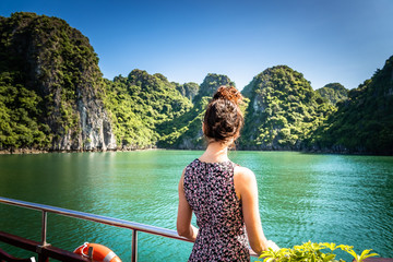 Young woman on a boat at the limestone rocks of Halong Bay / bai tu long bay, Vietnam.