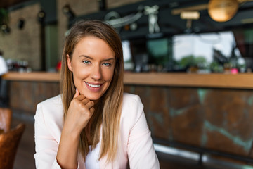 Beautiful business lady is looking at camera and smiling while working. Young businesswoman sitting at desk and working. Smiling and looking back at camera. Casual business woman