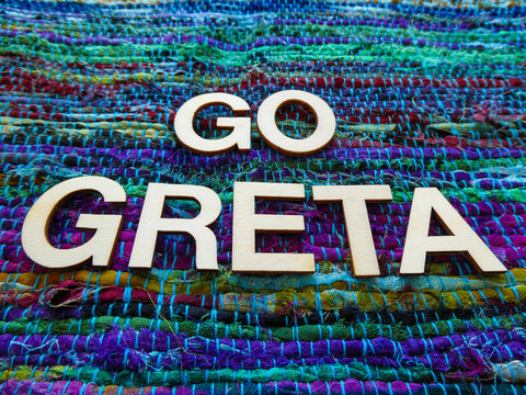Wooden text letters with the words "GO GRETA" for a sign, banner, placard or wallpaper on a vibrant green multicolor woven texture background