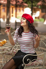 Woman in a red cap drinking red wine in outdoor cafe