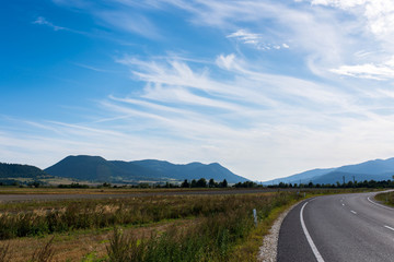 Empty asphalt road, vulcanic mountains against beautiful blue sky with white clouds near Tusnad Bai in Transylvania, Romania.