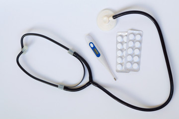 medical stethoscope with pills and thermometer on white background top view