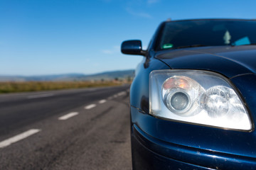 Japanese car headlight on focus near empty asphalt road at summertime .