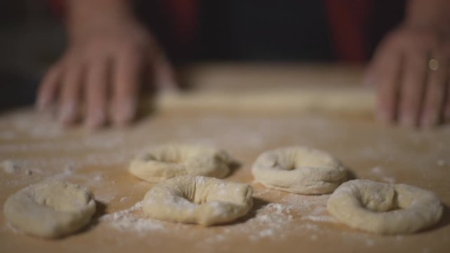 Woman chef preparing donuts bagels on a wooden table covered in flour. Close up, soft focus.