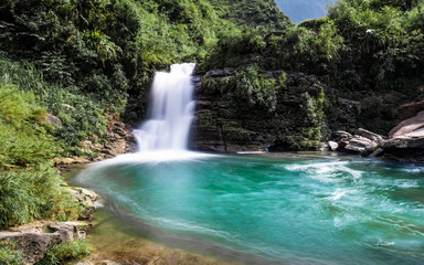 Fototapeta na wymiar Emerald green waterfall at Du Gia, at the Ha Giang loop in Northern Vietnam. Stunning landscape long exposure photo. 