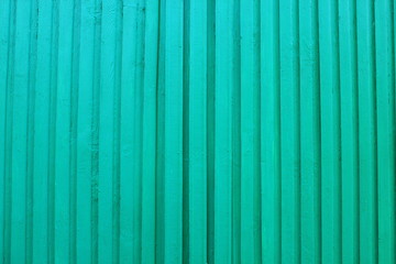 The green wall of the wooden house is made of vertical slats.