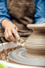 View at an senior female artist makes clay pottery on a spin wheel