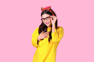 Beautiful woman with red headband and yellow dress touch eye glasses in front of pink background, also with concept of retro image.