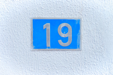19, number nineteen, blue metal plate on a white wall.