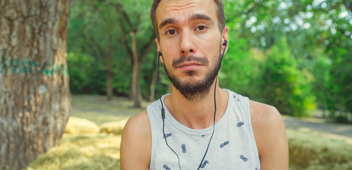 A young handsome man with beard in a t-shirt is sits in the hay, listens to music and sings in the...