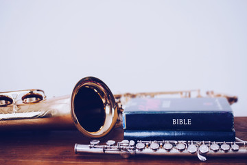 close up of stack of  bible with Saxophone and flute on wooden table over white wall texture...