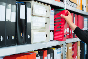 Mans hand picking a blank blind folder with files from the shelf. Archival, stacks of documents at...