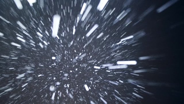 Night winter, heavy snow falls. The big snowflake shines in the strong light. Snowfall sometime faster sometime slower - various amount and intensity