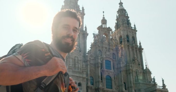 Portrait of happy male pilgrim looking at camera in Santiago de Compostela, Spanish town at the end of Camino de Santiago or Way of St James. Young man smiling in Spain, slow motion